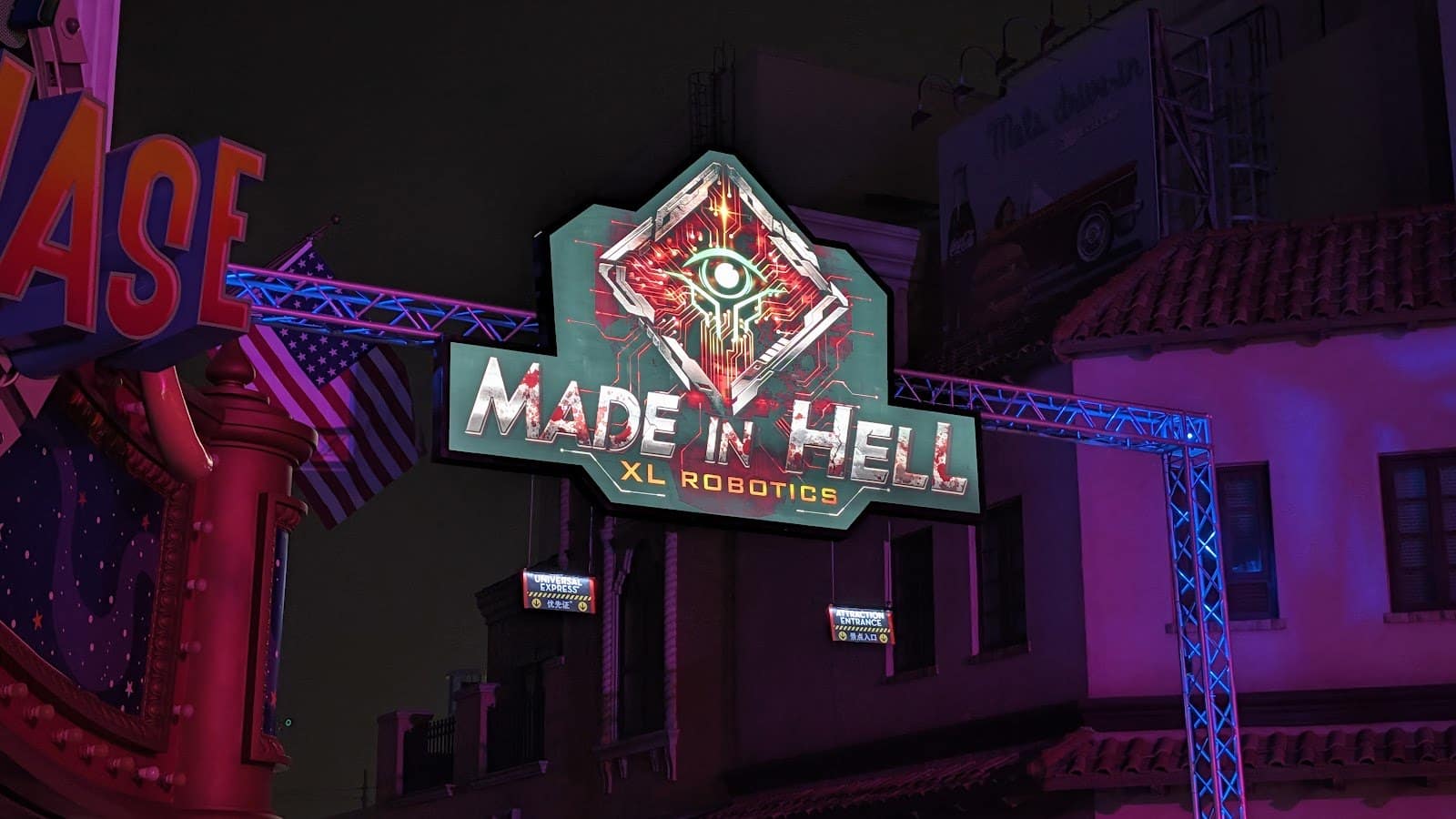 A diamond-shaped sign with a red mechanical eye hangs from a lighting truss over a street at night