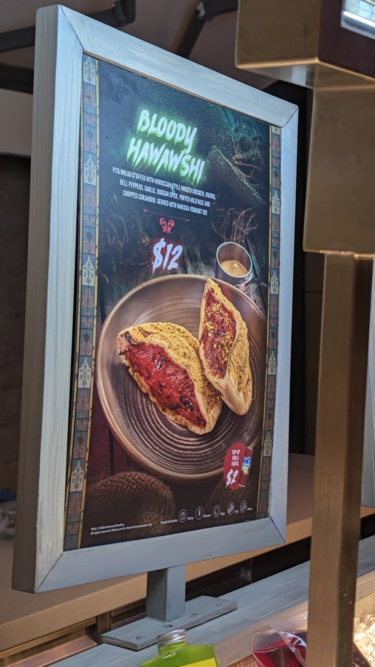 A framed menu sign picturing a stuffed pita with a red filling on a plate and a printed name and price
