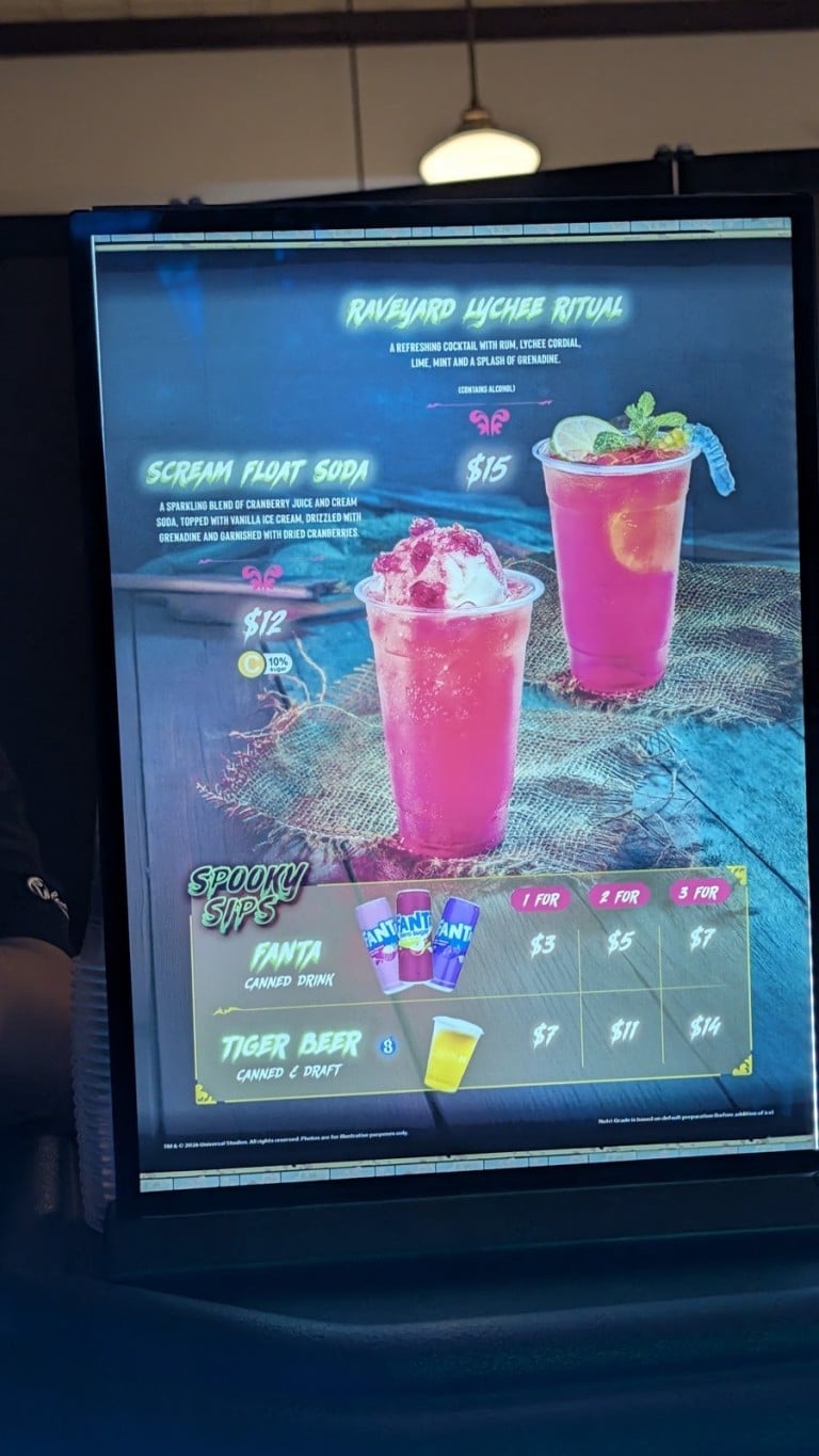 A lit drinks menu board picturing two pink iced drinks in clear cups with printed names and prices