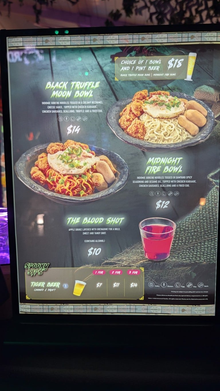 A lit menu board picturing two noodle bowls topped with fried chicken and a fried egg, a red shot, and a beer price table