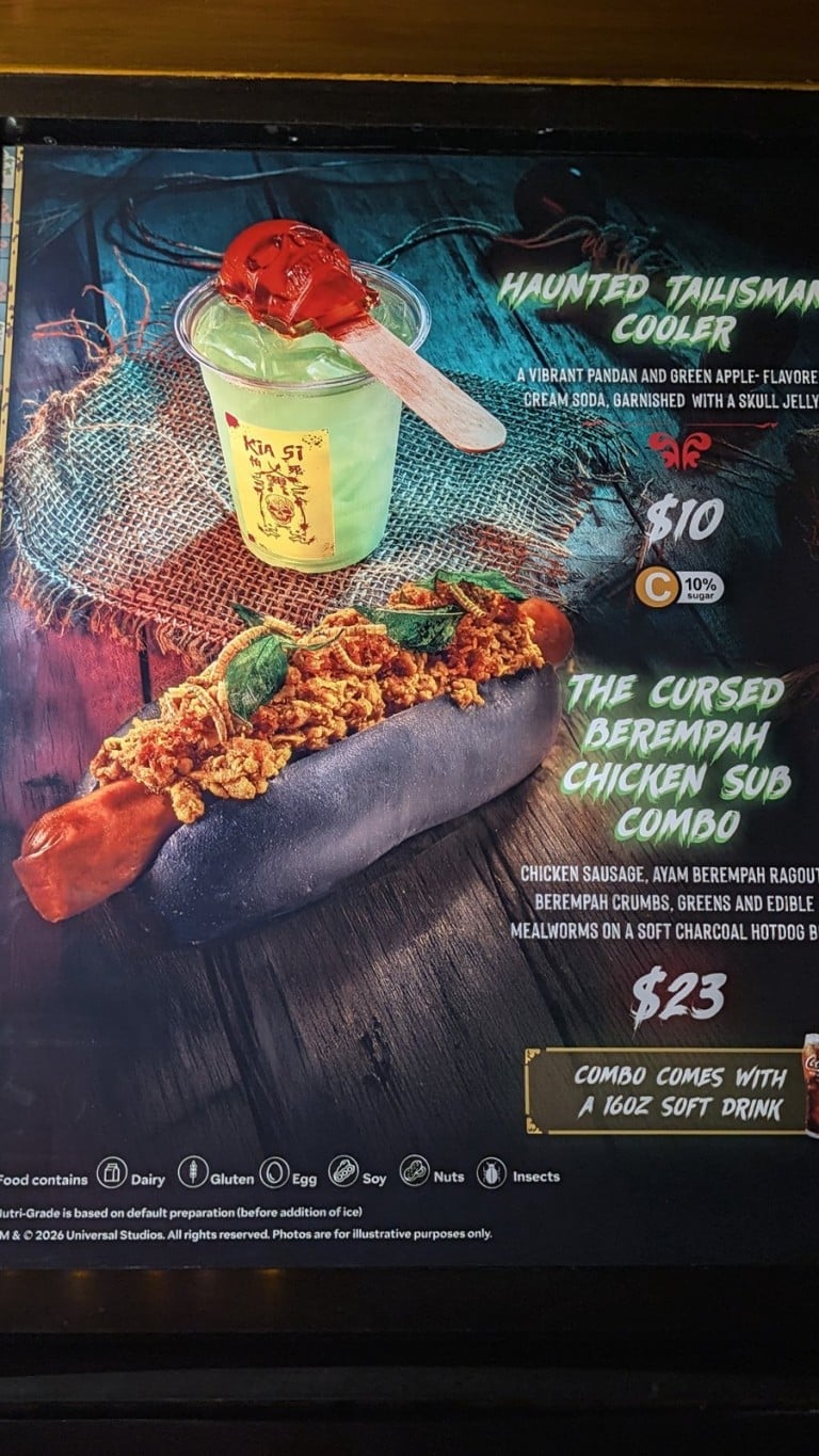 A lit menu board picturing a green drink in a cup and a hot dog on a black bun, each with a printed name and price