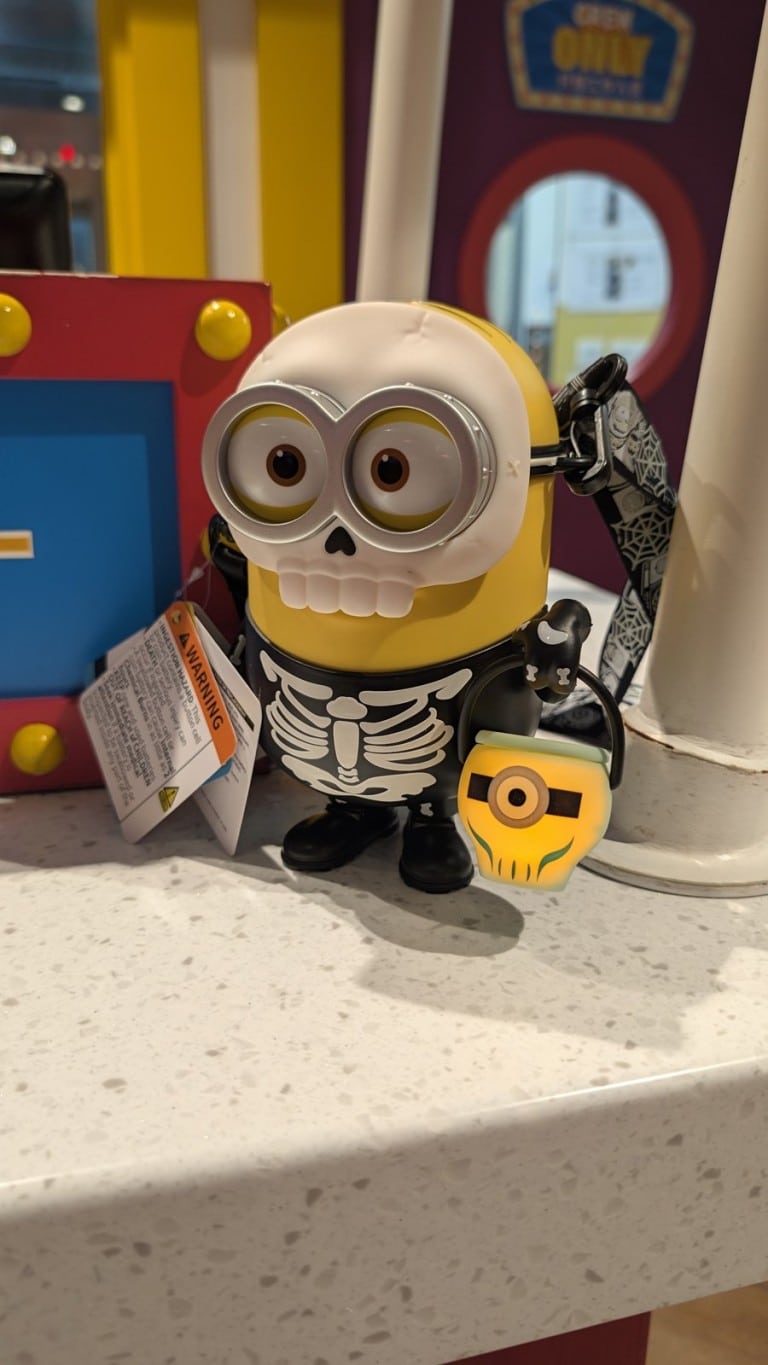 A yellow cartoon character cup in a skeleton suit with a skull face, on a counter