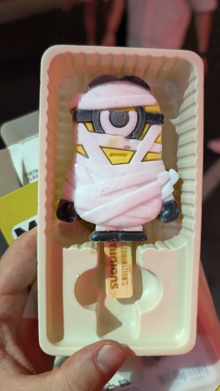 An ice cream bar shaped like a one-eyed cartoon character wrapped in bandages, in a plastic tray