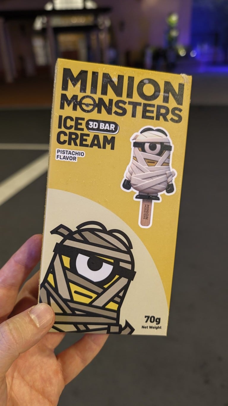 A hand holds a yellow ice cream bar box printed with a cartoon character wrapped in bandages