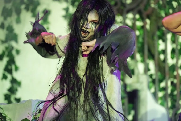 A dancer with long black hair over her face reaches forward with gray clawed hands