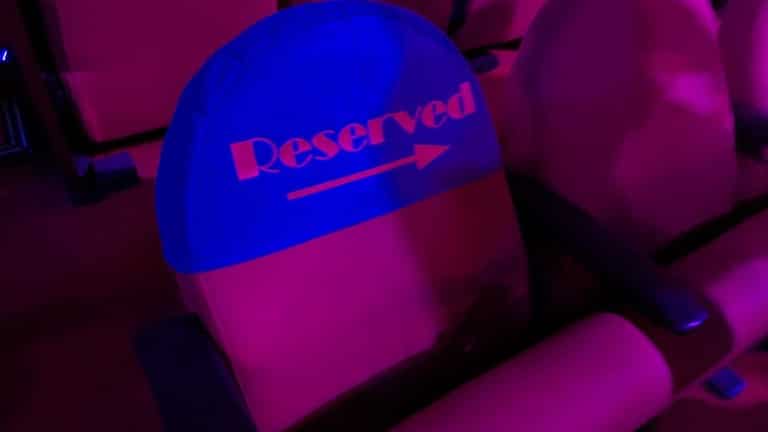 A theater seat with a cloth cover printed with one word and an arrow, in pink and blue light