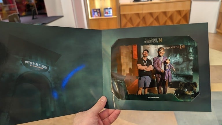 A hand holds open a card folder with a printed photo of two people and a puppet inside