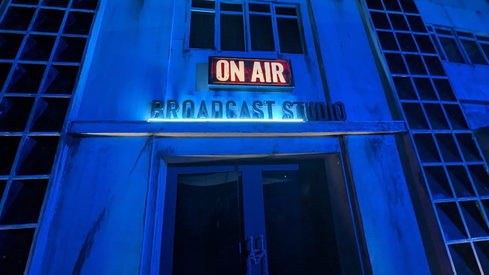 A building front lit blue with a red lit box sign above a dark doorway