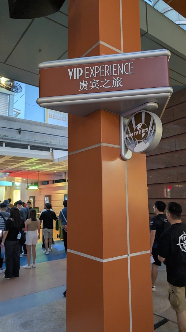 A sign on an orange pillar with English and Chinese lettering, with a covered walkway behind