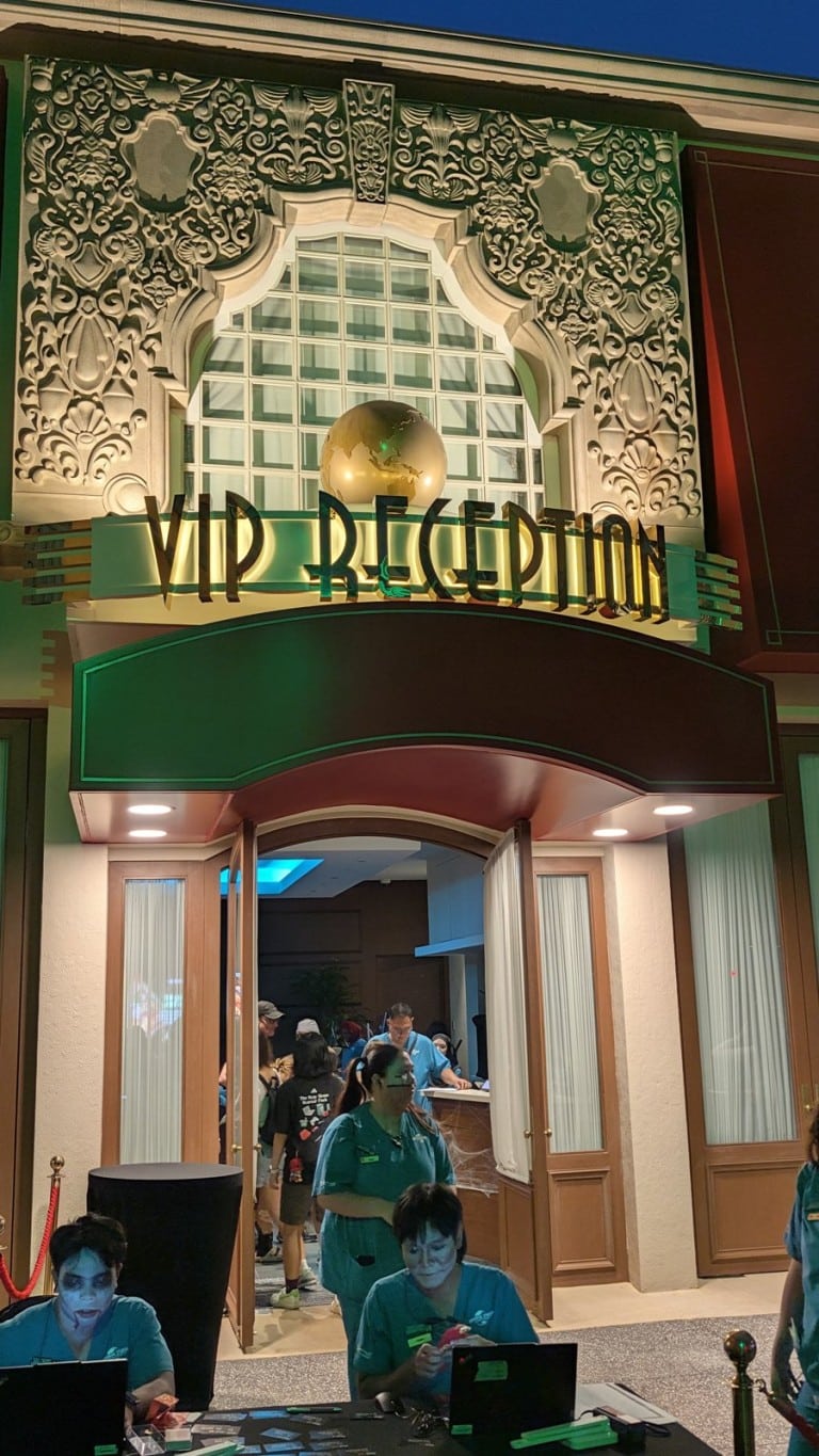 A tan building entrance with gold art deco lettering over the door and staff at a desk outside