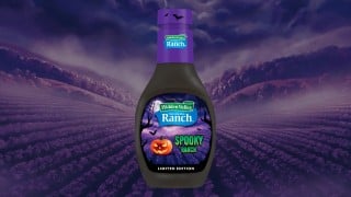 A bottle of Hidden Valley Spooky Ranch, black ranch dressing with a purple cap and a jack-o'-lantern label, over a purple valley at night