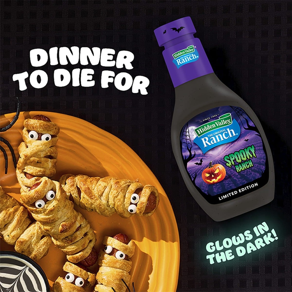 Mummy hot dogs wrapped in dough on an orange plate beside a bottle of Hidden Valley Spooky Ranch