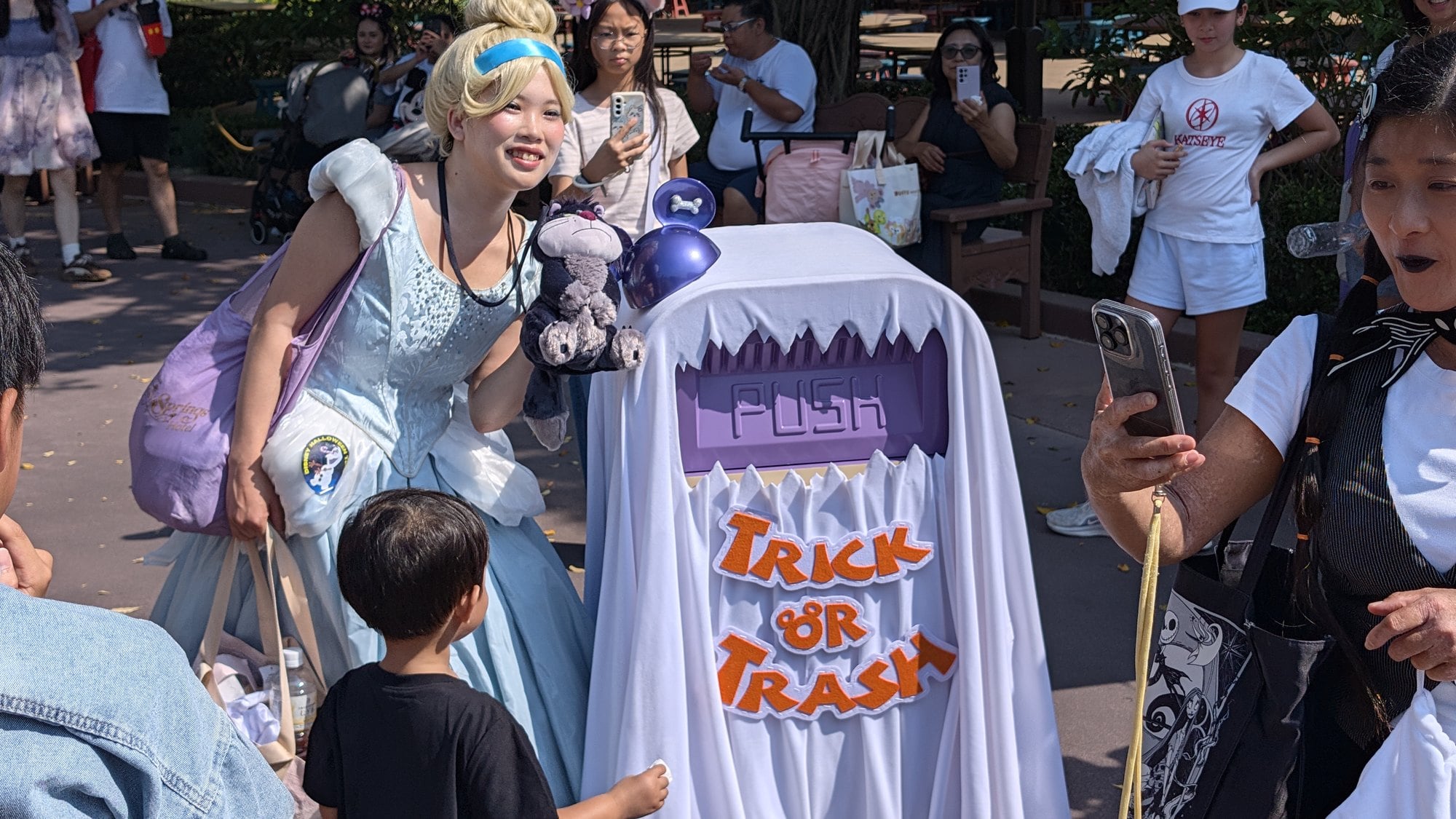 A guest dressed as Cinderella poses beside a Trick or Trash ghost bin as other guests take photos at Hong Kong Disneyland