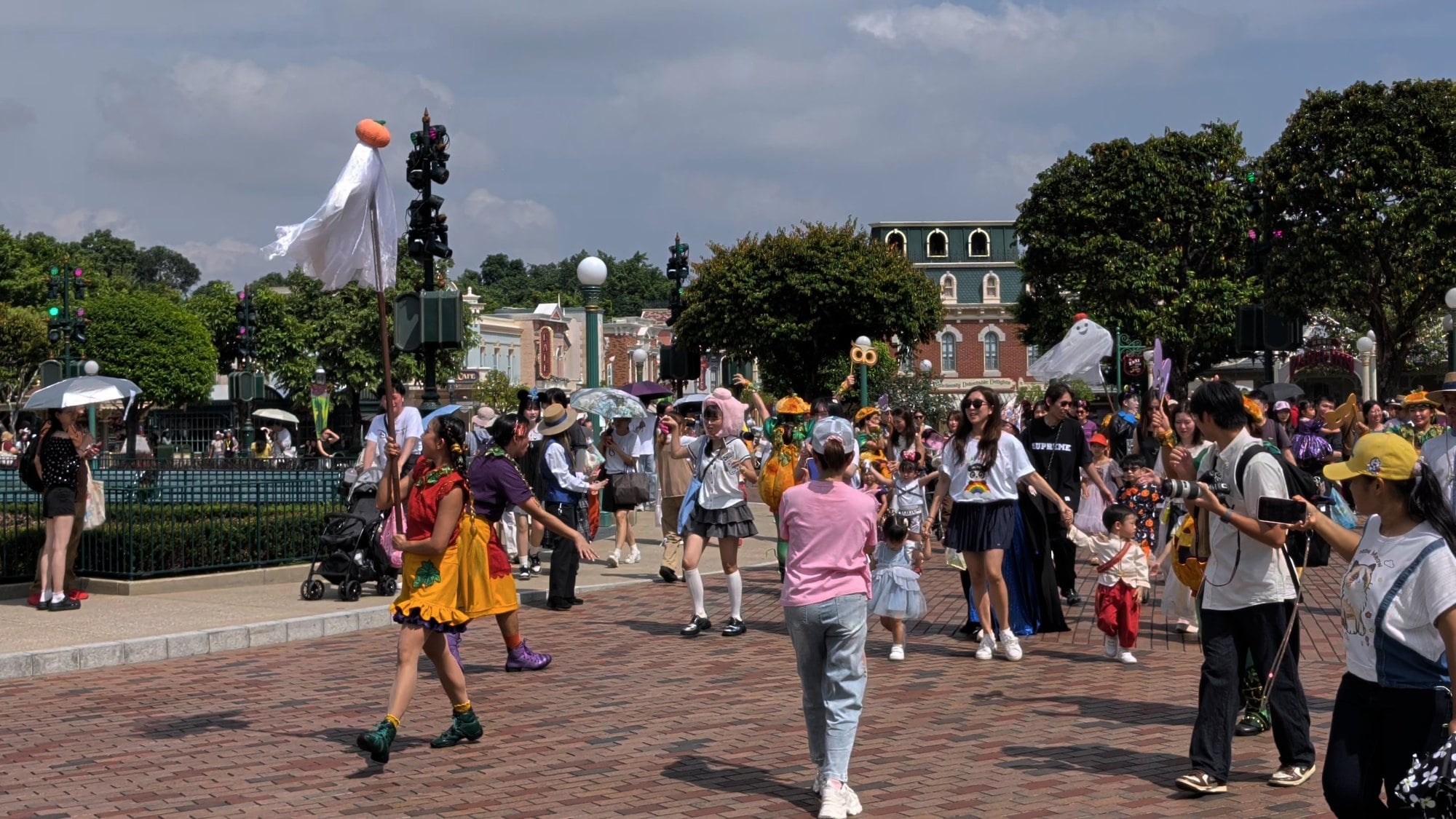 Adults and children, some in costume, walk in a parade through the plaza in front of the castle at Hong Kong Disneyland