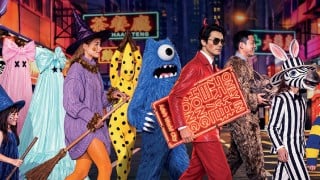People in Halloween costumes, including a witch, a blue one-eyed monster, a man in a red suit with devil horns, and a zebra, crossing a neon-lit Hong Kong street