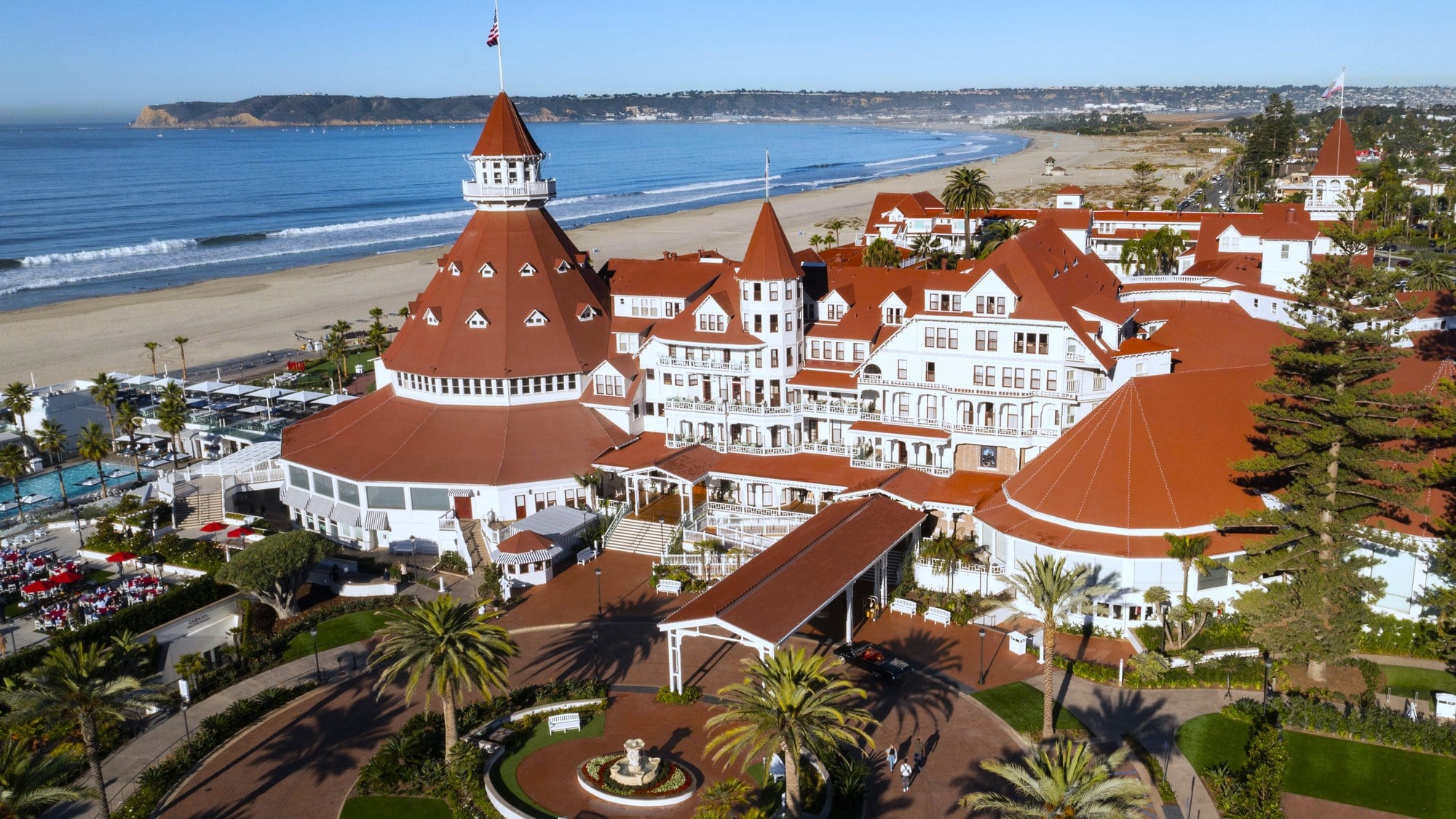 Aerial view of Hotel del Coronado's red-roofed Victorian buildings beside the beach and the Pacific Ocean