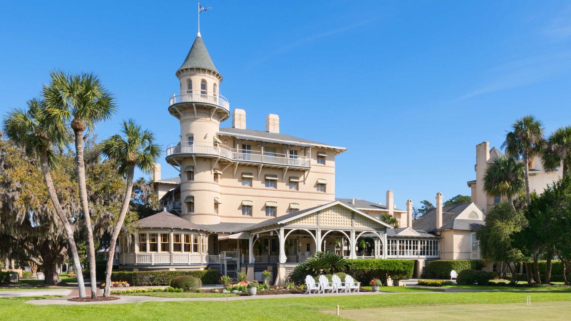 The turreted clubhouse of Jekyll Island Club Resort with palm trees and white lawn chairs under a blue sky