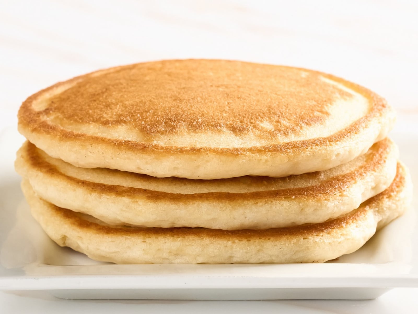 A stack of four buttermilk pancakes on a white plate