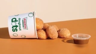 Krispy Kreme Churro Doughnut Dots spilling from a Doughnut Dots cup beside a cup of dulce de leche dipping sauce