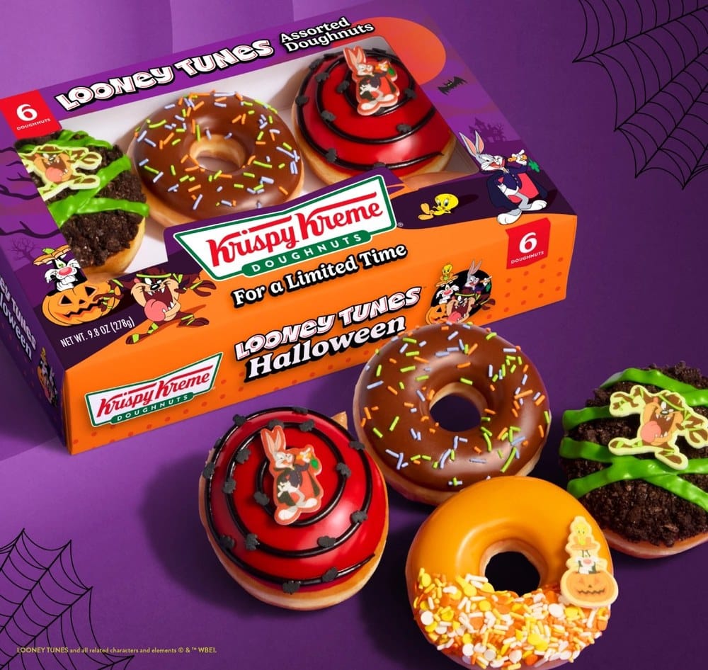 A Krispy Kreme Looney Tunes Halloween six-count box beside four of its doughnuts on a purple background