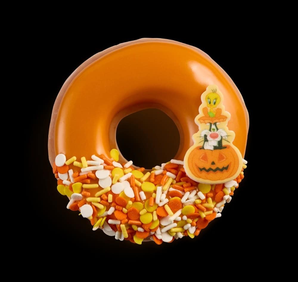 A ring doughnut with orange icing, candy corn colored sprinkles, and a sugar piece of Tweety and Sylvester in a jack-o'-lantern