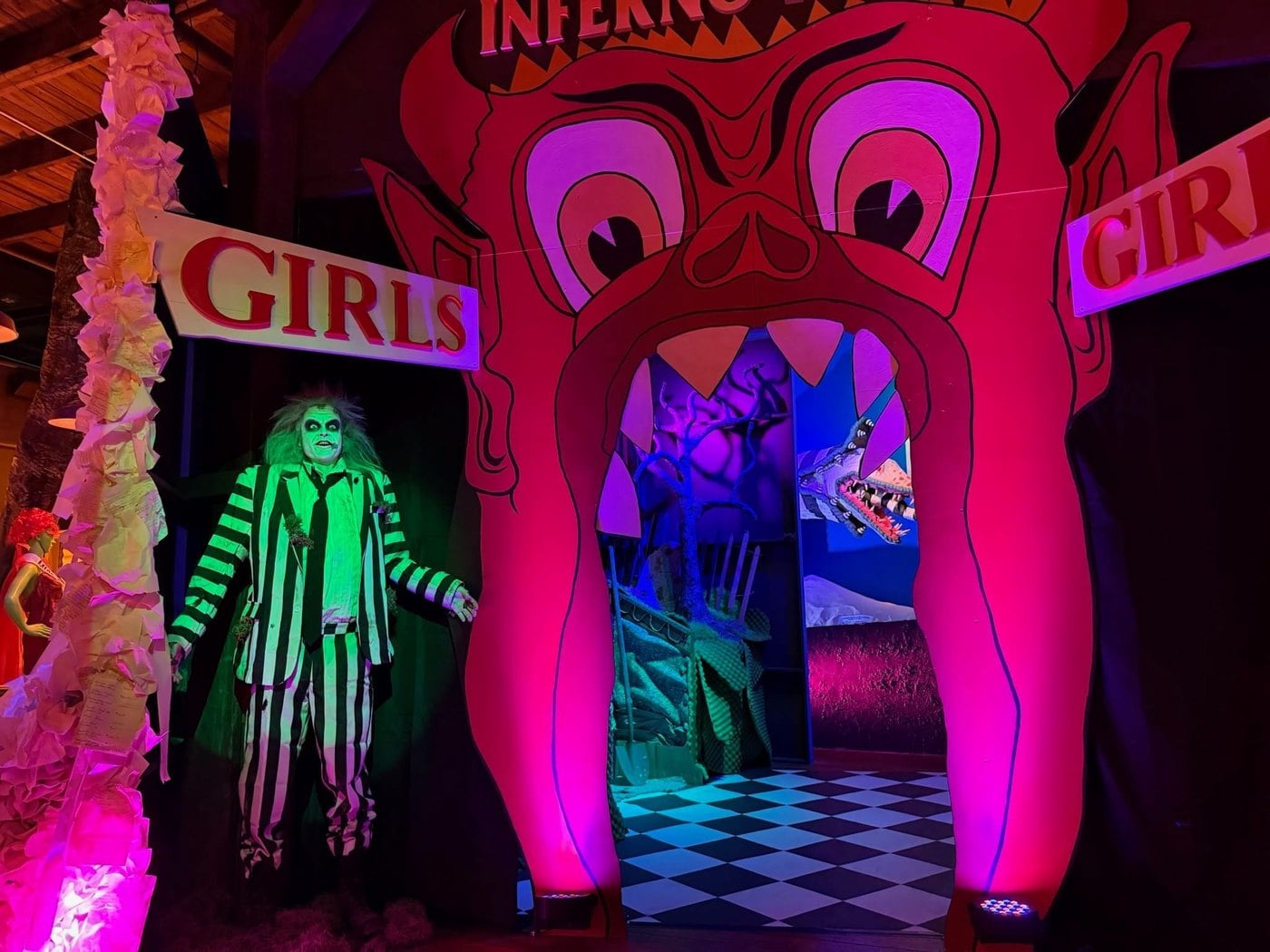 A red monster-face arch lettered Inferno with Girls signs, a green-lit Beetlejuice figure beside it, and the sandworm visible through its mouth