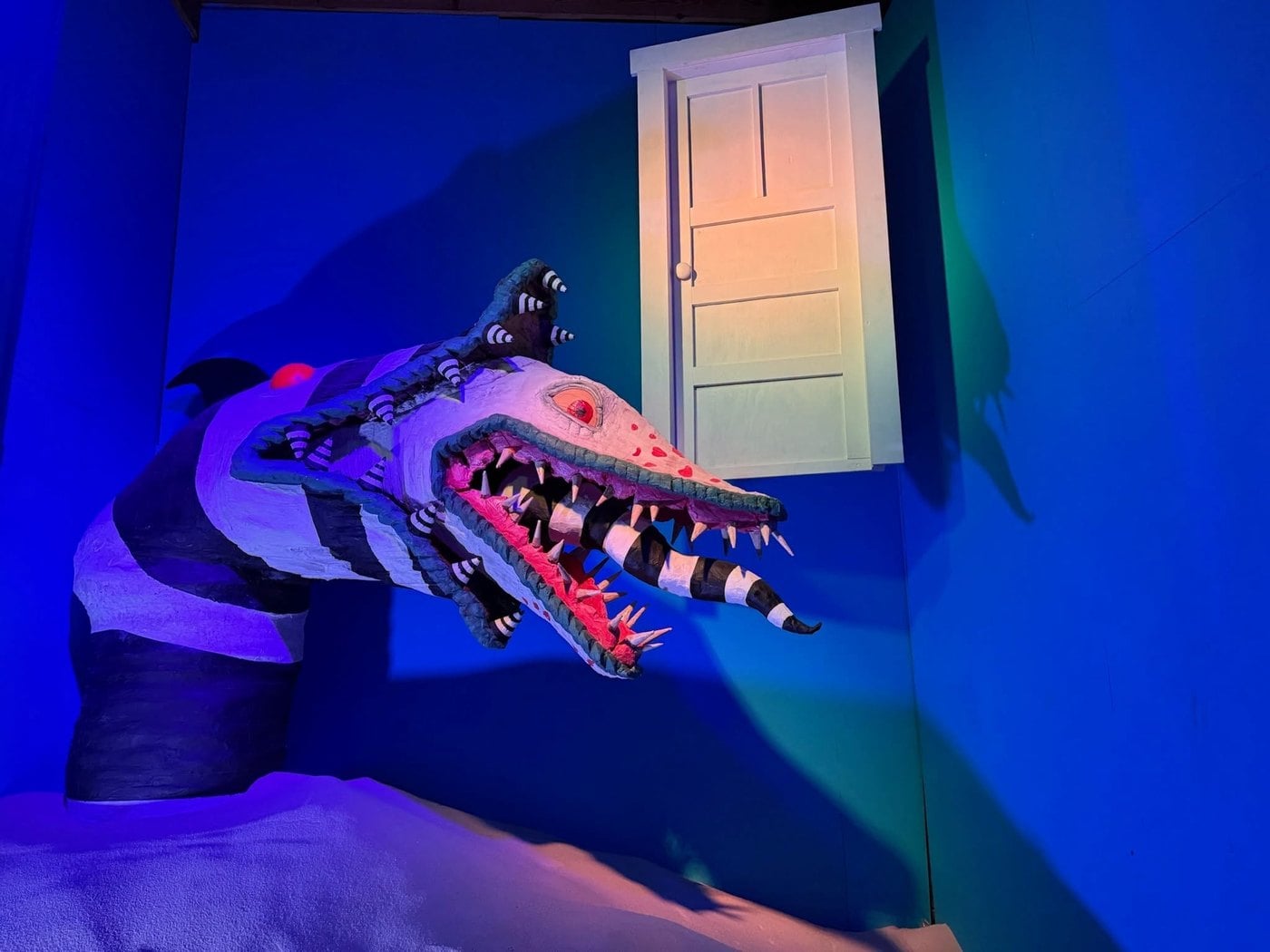 A black-and-white striped sandworm bursting out of a blue wall beside a white door at The Lucky Rabbit