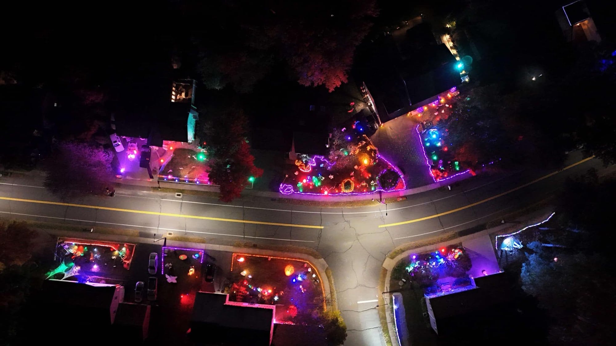 An aerial view at night of lit, decorated front yards along both sides of a curving street