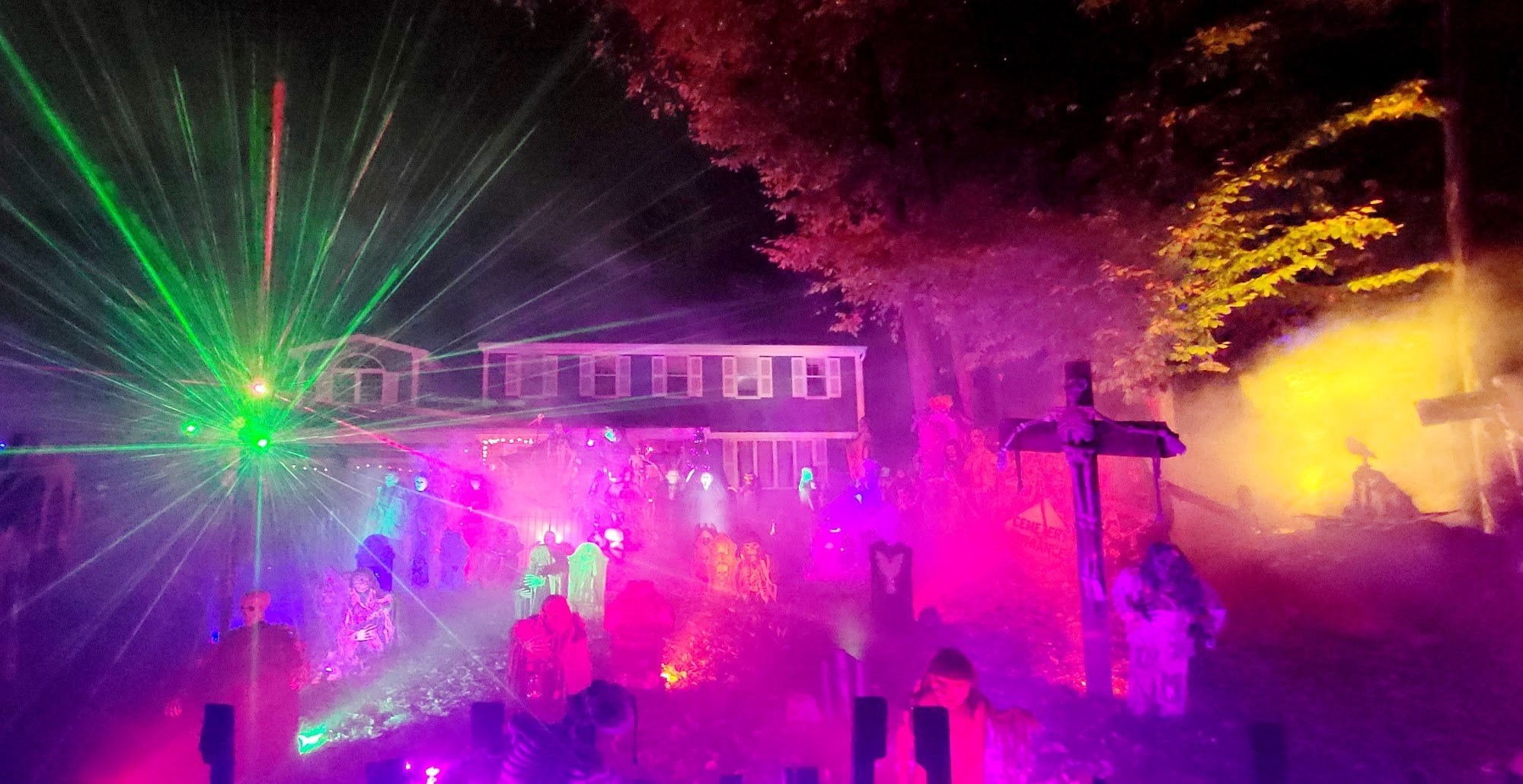 Green lasers and pink fog over a decorated front yard and a house at night