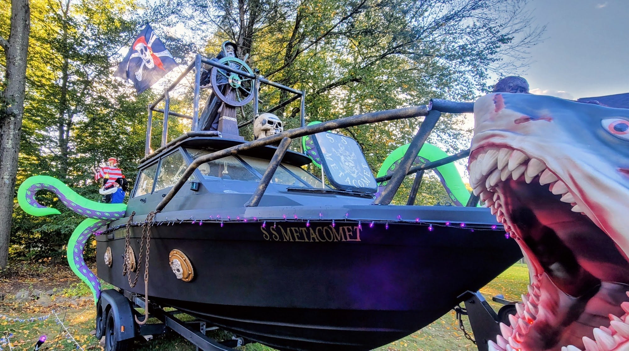 A boat painted black as a pirate ship named S.S. Metacomet, with a skeleton at the wheel, green tentacles and a shark head, on a front lawn