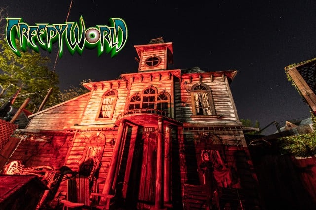 A weathered two-story wooden house with a cupola, lit red at night
