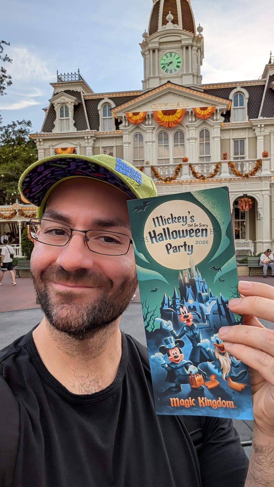 Philip Hernandez holding the 2026 Mickey's Not-So-Scary Halloween Party guide map in front of City Hall at Magic Kingdom