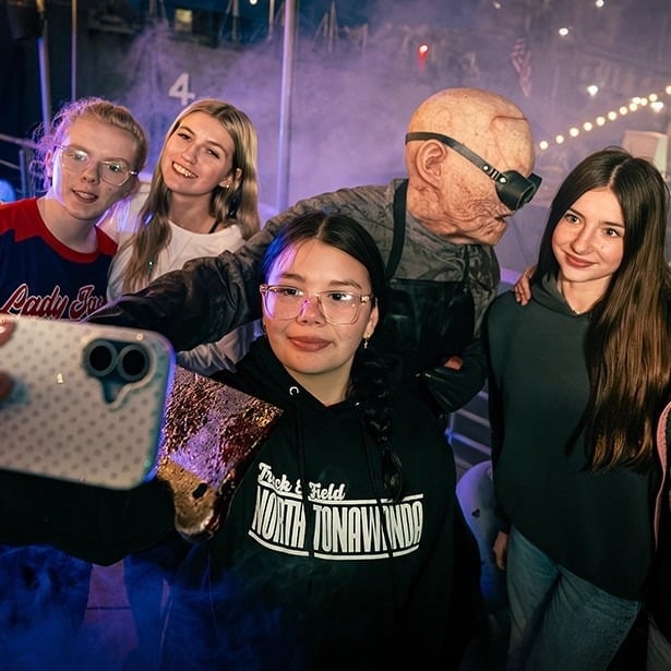 Four guests take a selfie with a Nightmare Wharf character in goggles on the waterfront