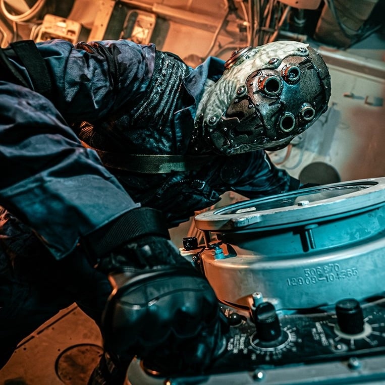 A Nightmare Wharf performer in a riveted metal mask leans over ship machinery