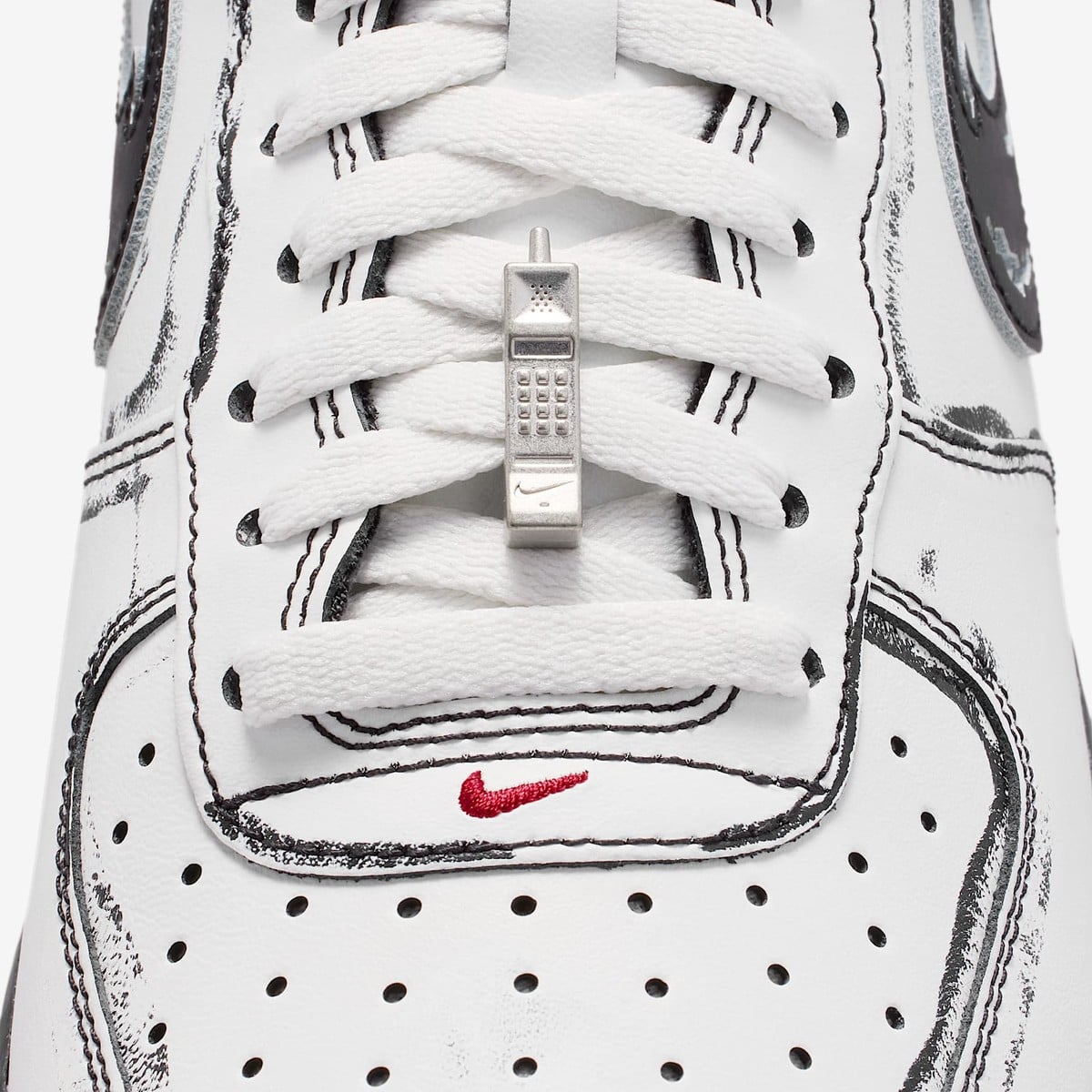 A small silver cordless-phone charm hanging on the white laces of the Air Force 1
