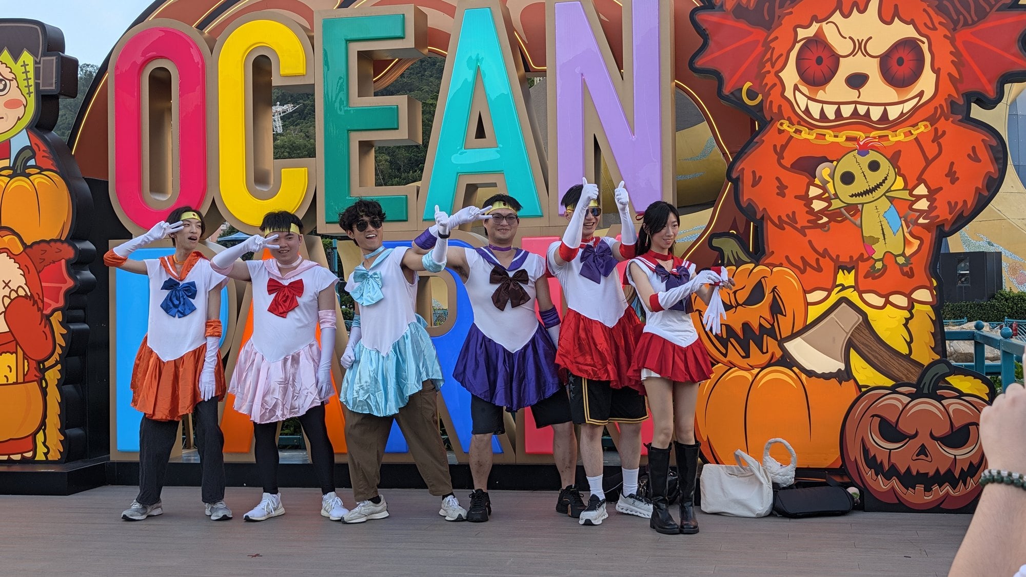 Six guests in matching sailor-suit costumes pose in front of the Ocean Park sign and a Halloween monster backdrop