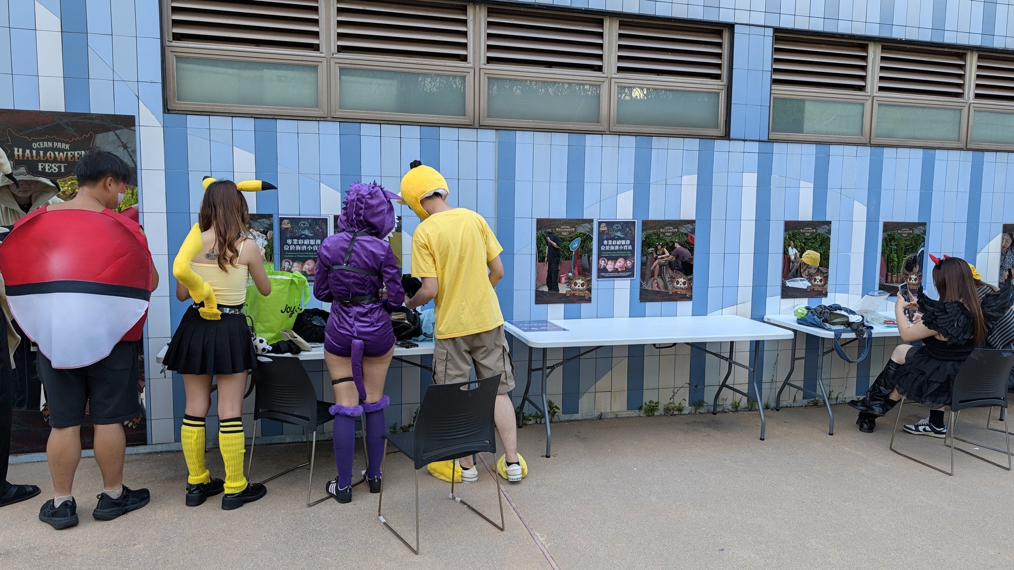 Guests in costumes, including a Pikachu and a Poke Ball, stand at a row of makeup and costume tables at Ocean Park Hong Kong
