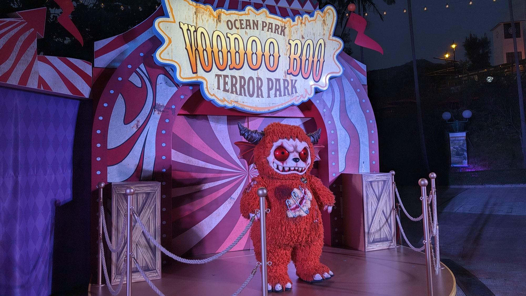 Voodoo Boo, a furry red monster character, stands on a circus-themed photo stage under a Voodoo Boo Terror Park sign
