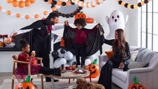 A family in Halloween costumes surrounded by Party City Halloween balloons, a ghost balloon, and jack-o'-lantern decorations