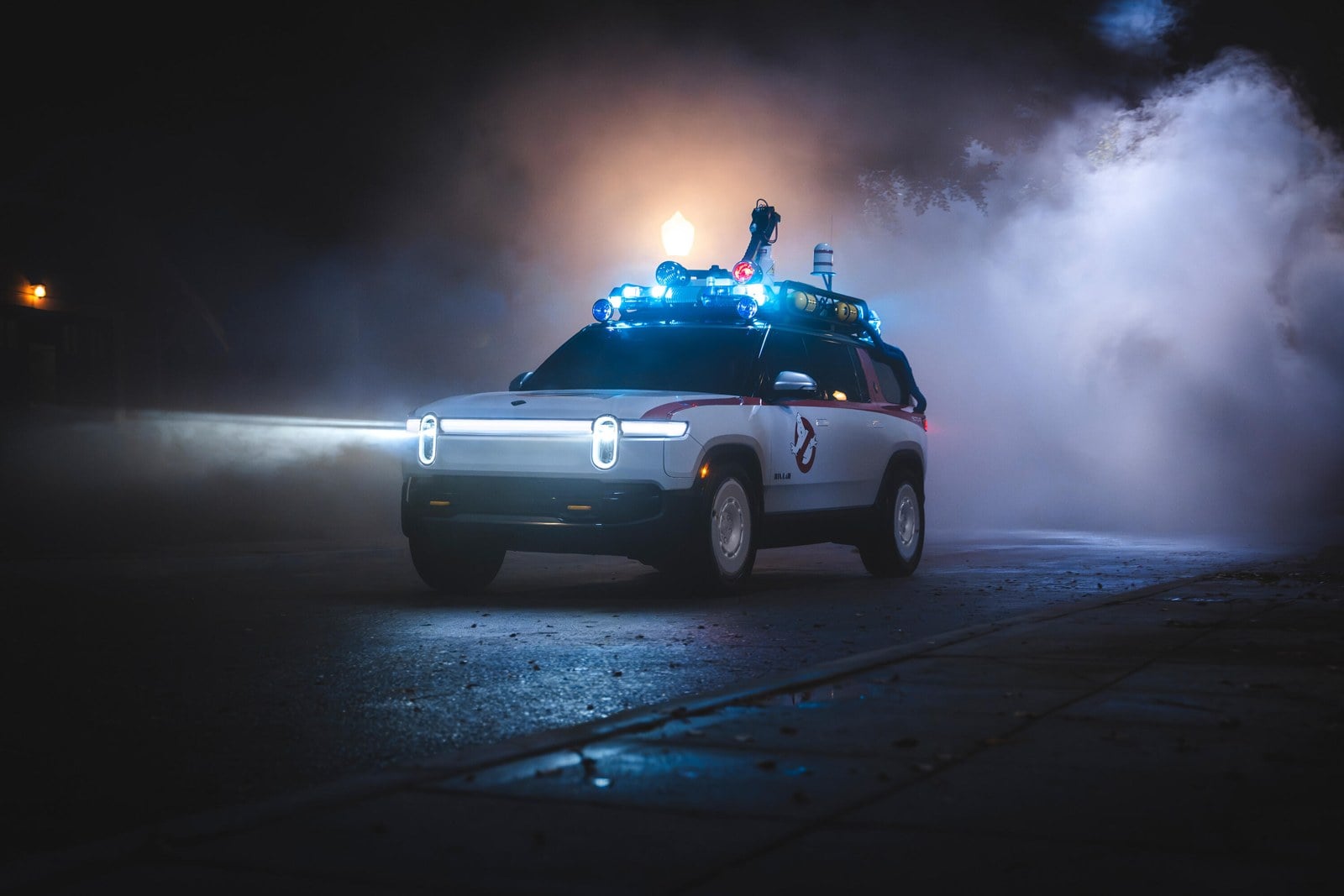 A white vehicle with a glowing headlight bar and blue lights on its roof drives through fog at night