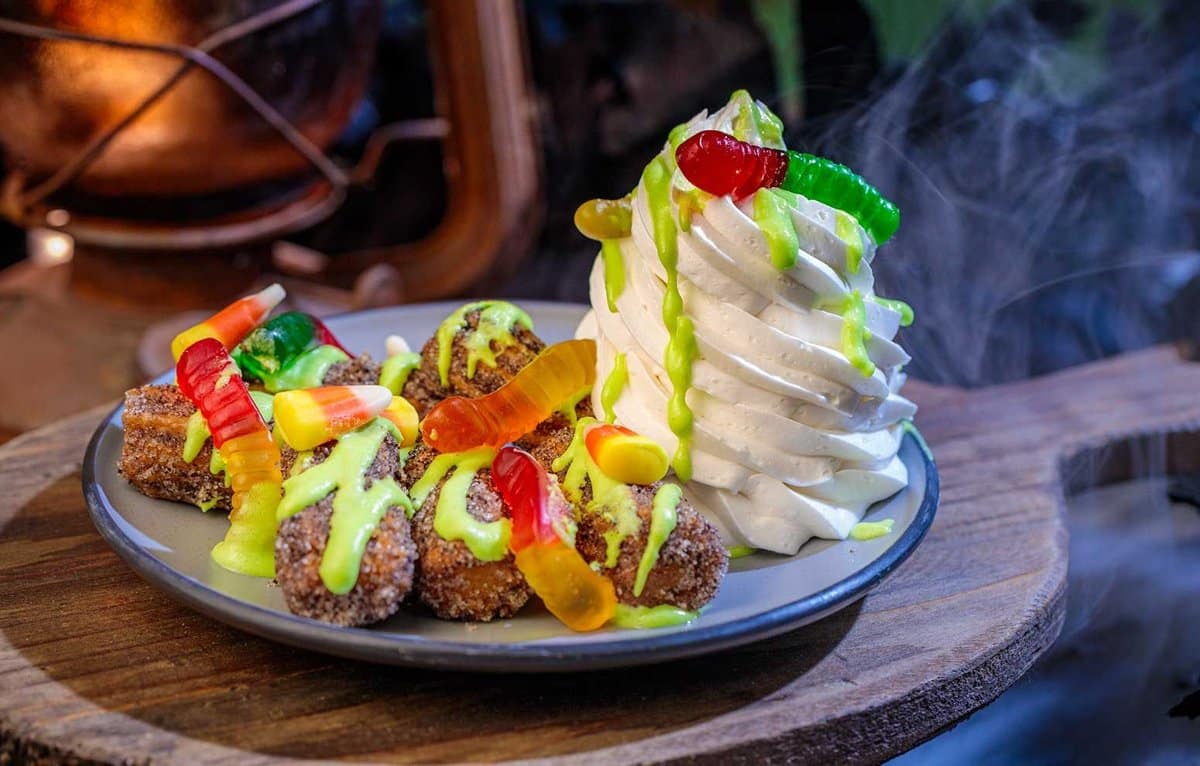 Mini churros with green icing and gummy worms beside whipped cream