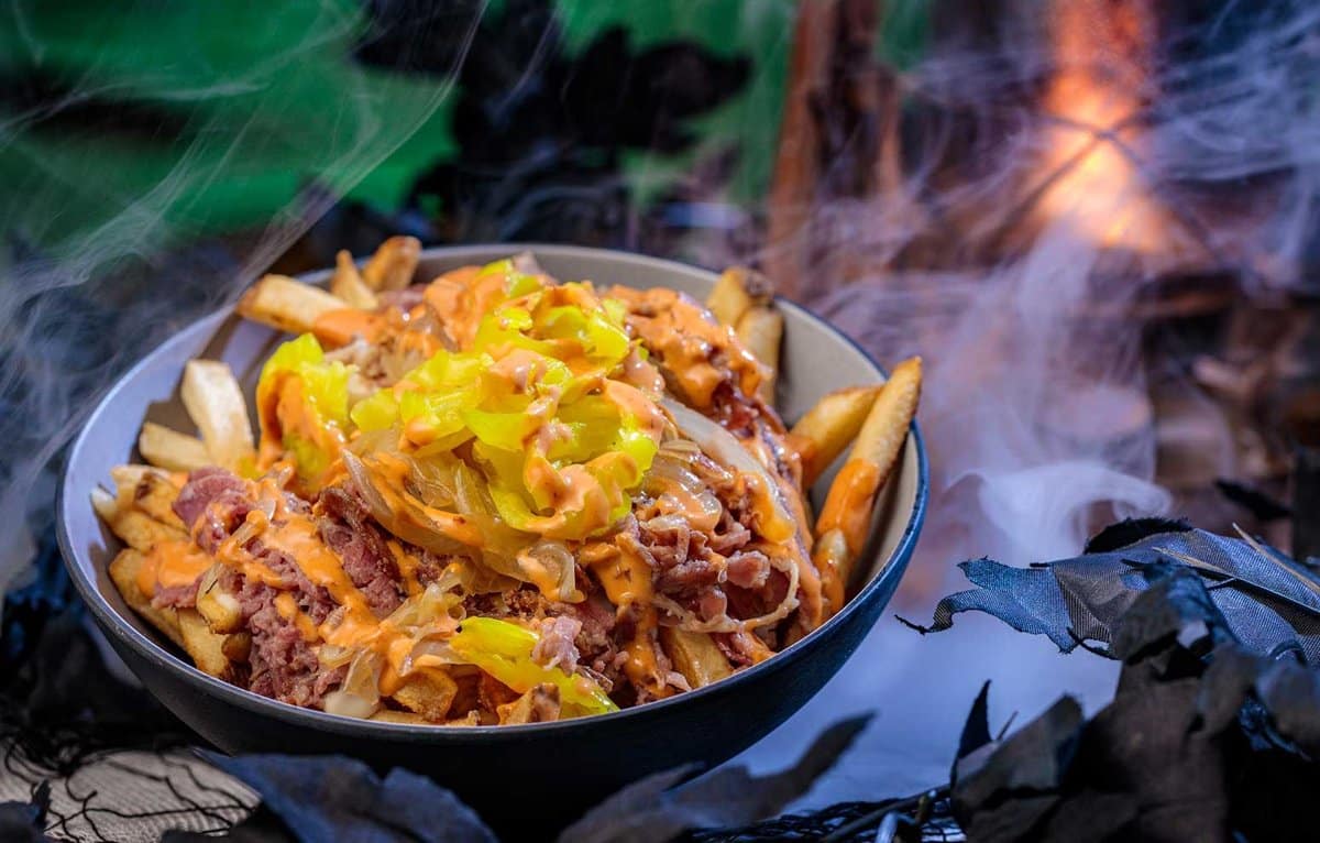 A bowl of fries topped with shaved pastrami, cheese sauce, grilled onions, and banana peppers