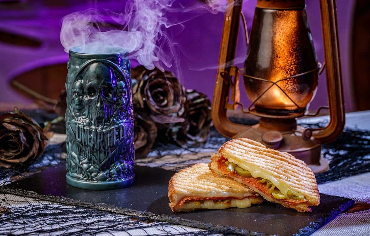 A toasted panini beside a teal skull tiki mug that reads Unearthed