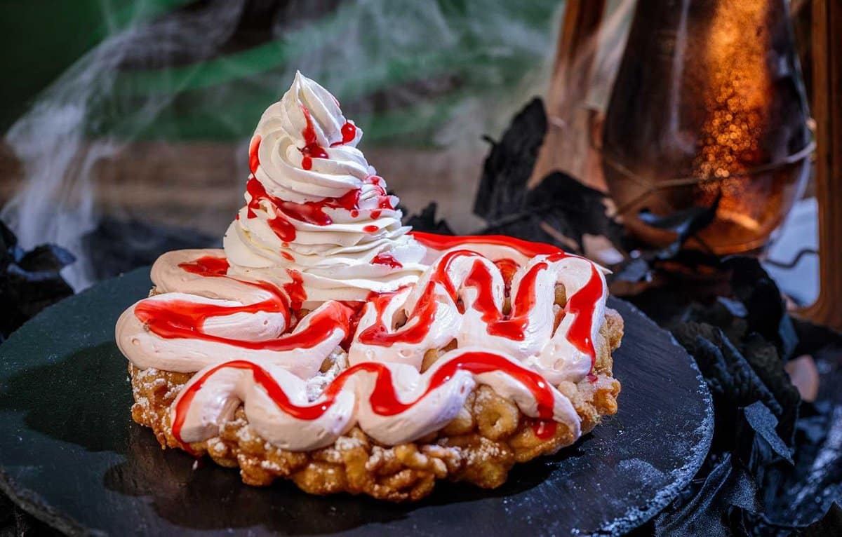 A funnel cake with pink whipped cream and red raspberry sauce