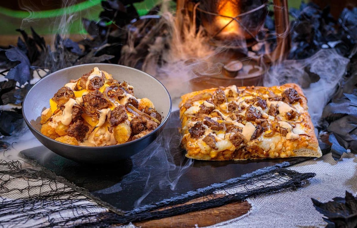A bowl of loaded tater tots beside a square slice of loaded pizza