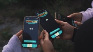 Two hands hold up phones running the Scream Score app at night, one screen showing 103 and the other 79