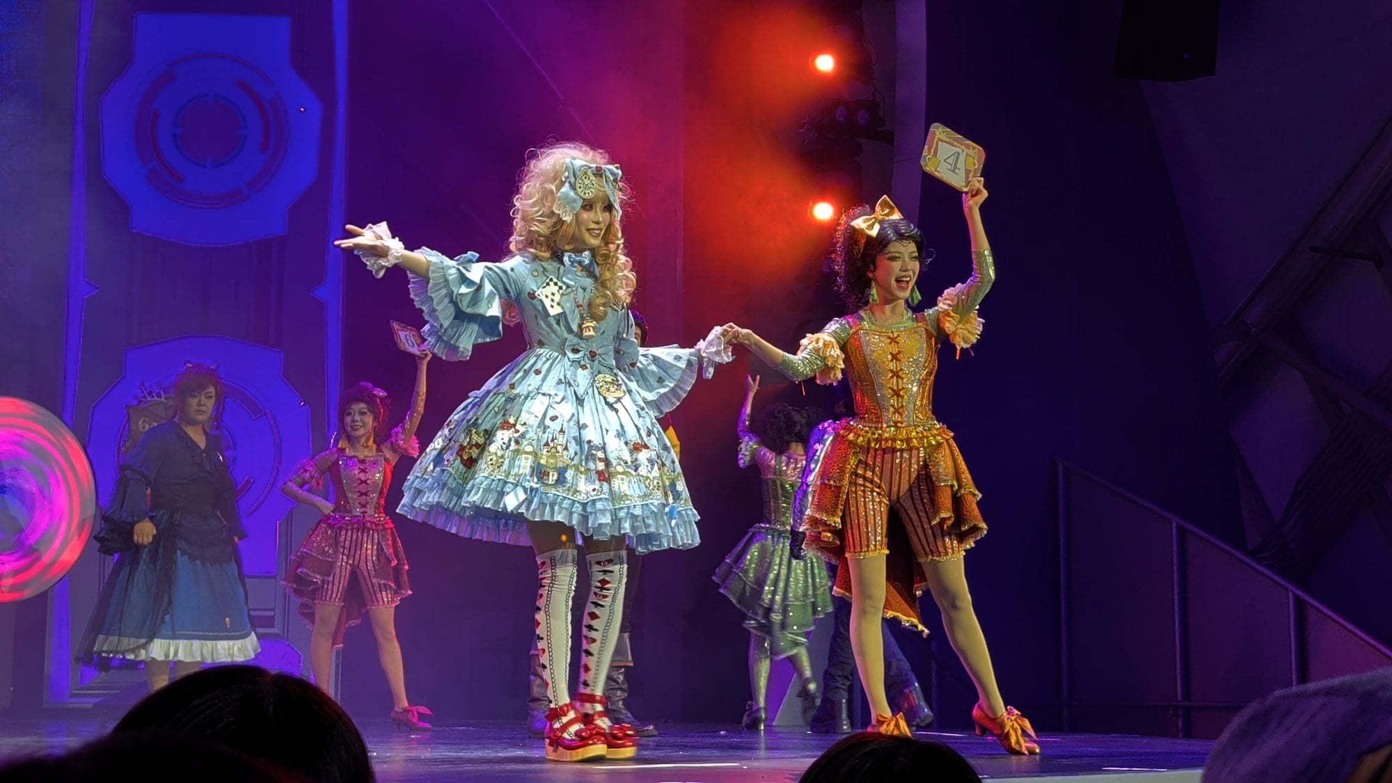 Two guests in elaborate costumes pose on stage, one holding up a number card, during The Villains' Club at Shanghai Disneyland
