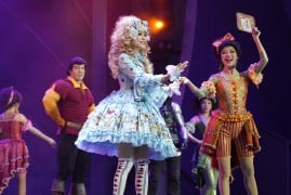 Two guests in elaborate costumes stand on stage beside a performer dressed as Gaston during The Villains' Club show at Shanghai Disneyland