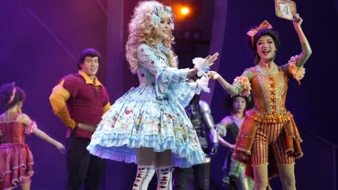 Two guests in elaborate costumes stand on stage beside a performer dressed as Gaston during The Villains' Club show at Shanghai Disneyland