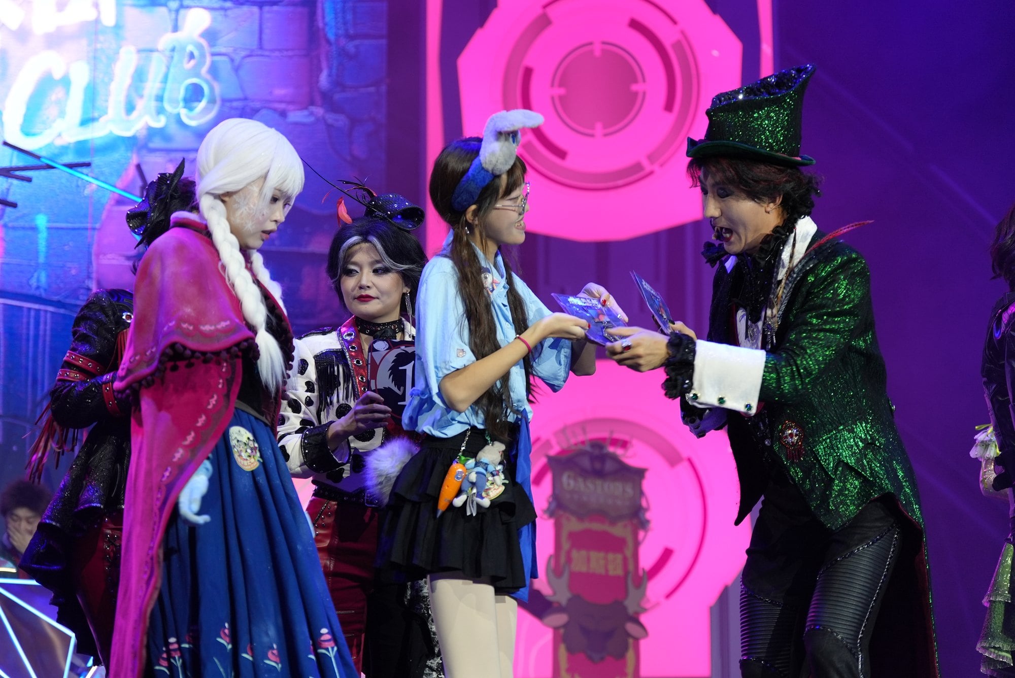 A performer in a green sequined jacket hands a prize to a guest on stage among other costumed guests